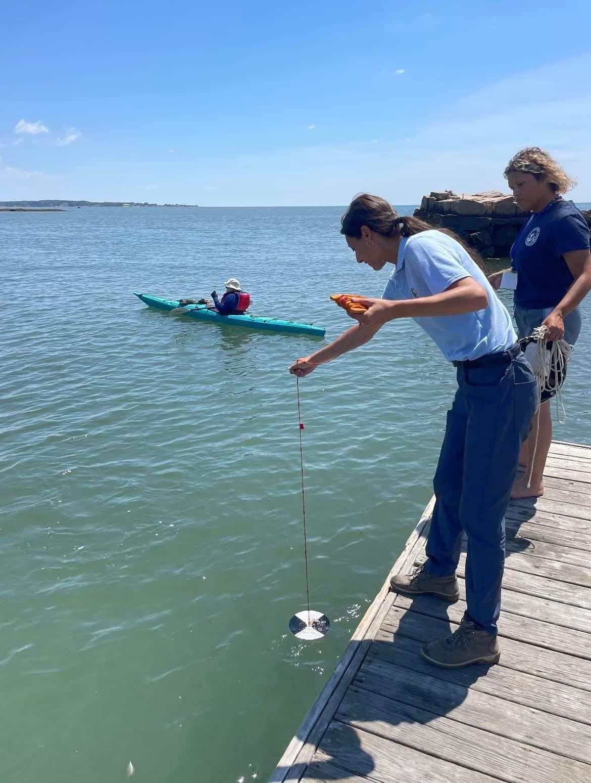 Woman on pier holding cord over water with instrument attached